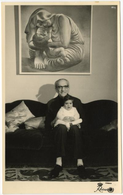 Almada com a primeira neta, Rita, ao colo, por baixo do seu quadro <em>Maternidade</em> (1935).